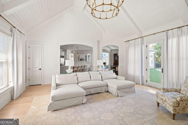 living room with beamed ceiling, arched walkways, an inviting chandelier, and light wood finished floors