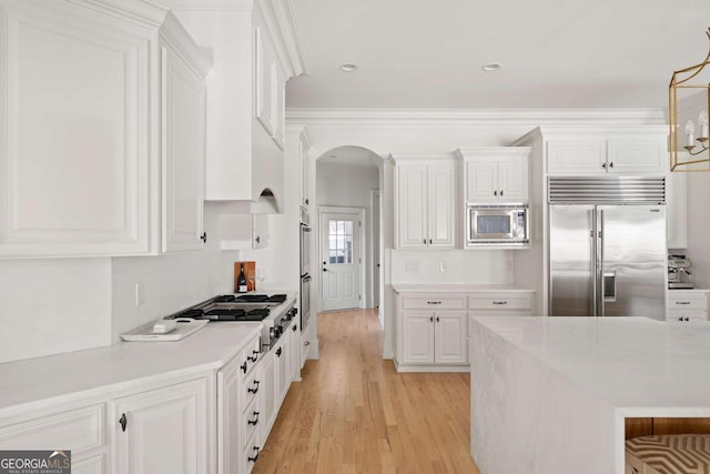 kitchen with light wood finished floors, built in appliances, light countertops, arched walkways, and white cabinetry