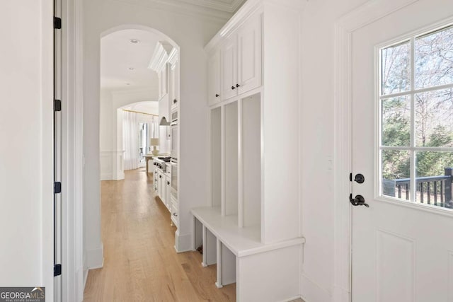 mudroom featuring light wood-type flooring, arched walkways, and a decorative wall