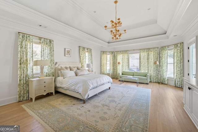 bedroom featuring a chandelier, light wood-style flooring, a raised ceiling, and ornamental molding