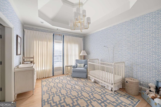 bedroom featuring wallpapered walls, a raised ceiling, light wood-style flooring, and a notable chandelier