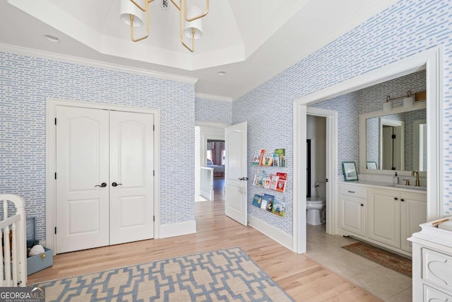 bedroom with light wood-style flooring, a sink, crown molding, wallpapered walls, and a raised ceiling