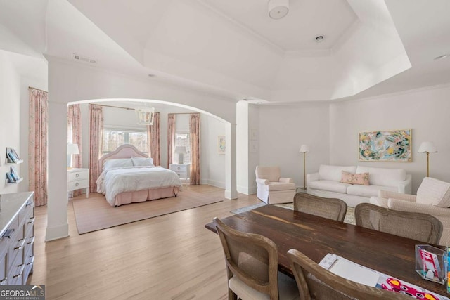 bedroom with visible vents, arched walkways, an inviting chandelier, light wood finished floors, and a raised ceiling