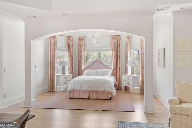 bedroom featuring visible vents, light wood finished floors, baseboards, arched walkways, and crown molding