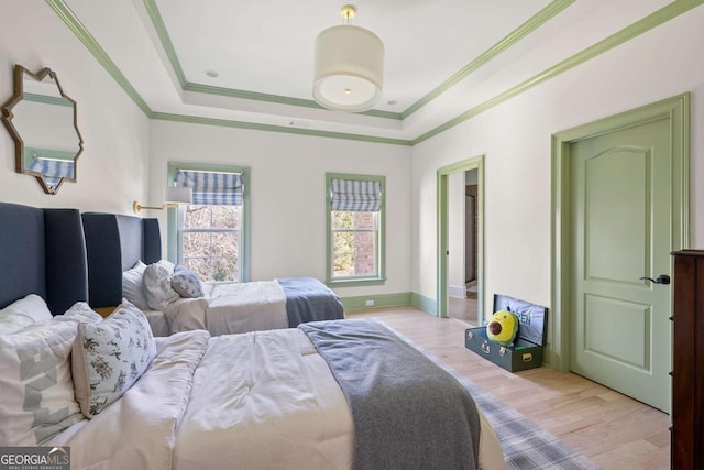 bedroom featuring baseboards, a raised ceiling, ornamental molding, and light wood finished floors