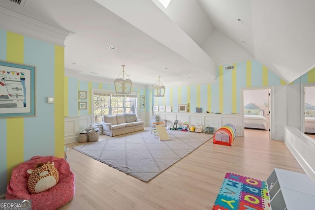 game room featuring wood finished floors, visible vents, lofted ceiling, wainscoting, and a decorative wall