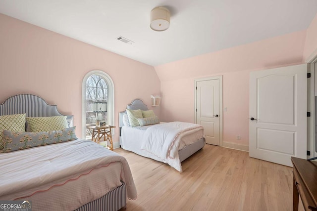 bedroom featuring visible vents, light wood-style flooring, baseboards, and lofted ceiling