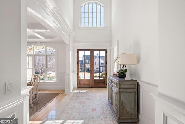 entrance foyer with french doors, coffered ceiling, a healthy amount of sunlight, and a wainscoted wall