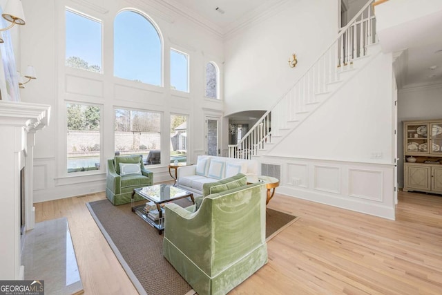 living room featuring crown molding, wood finished floors, stairs, and a decorative wall