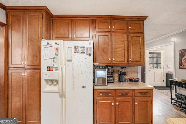 kitchen with a textured ceiling, light wood-style floors, white fridge with ice dispenser, brown cabinetry, and light countertops