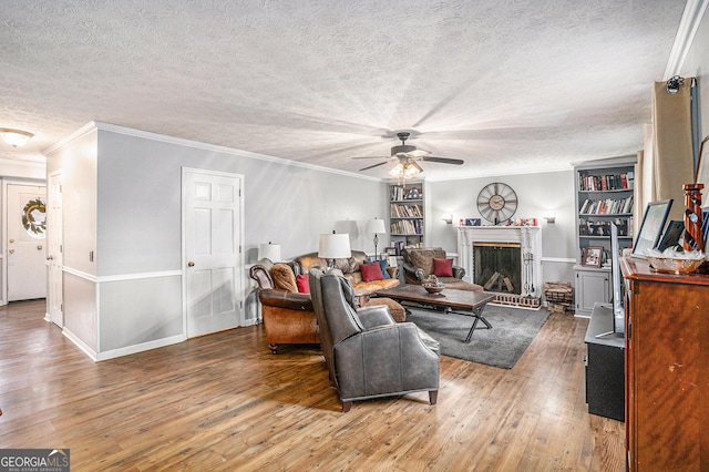 living room with built in shelves, crown molding, hardwood / wood-style flooring, a textured ceiling, and a ceiling fan