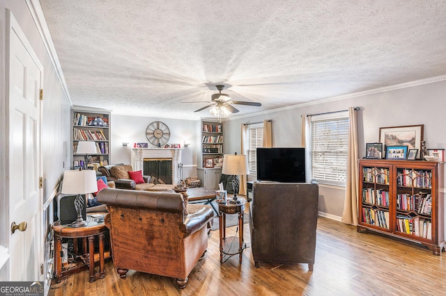 living area with crown molding, a fireplace, wood finished floors, a textured ceiling, and a ceiling fan