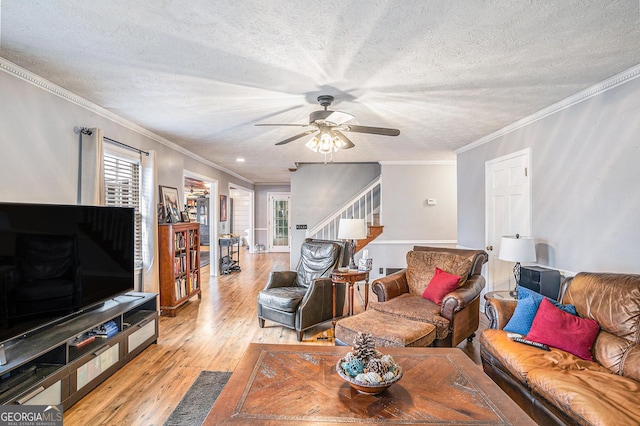 living room featuring stairway, a ceiling fan, light wood-type flooring, and a textured ceiling