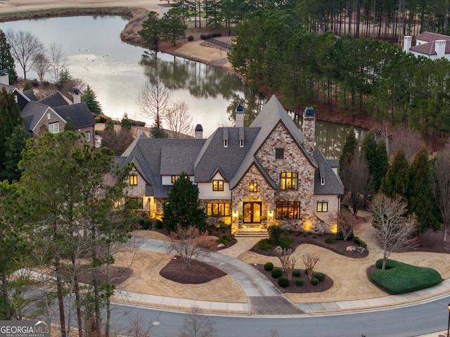 view of front of property featuring stone siding, curved driveway, a chimney, and a water view