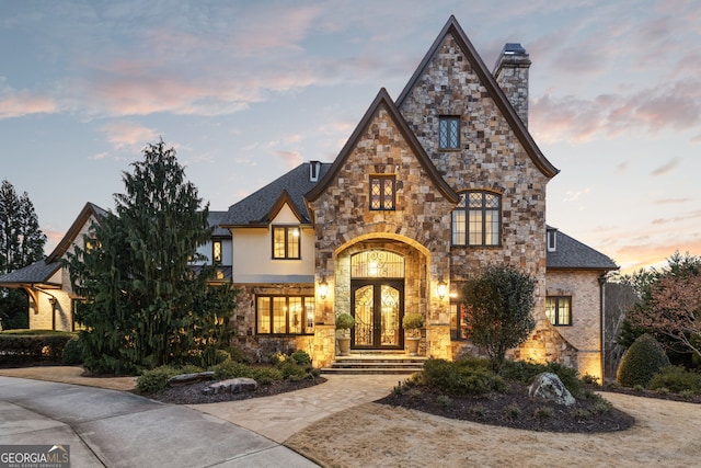 view of front of property featuring stone siding, french doors, and a chimney