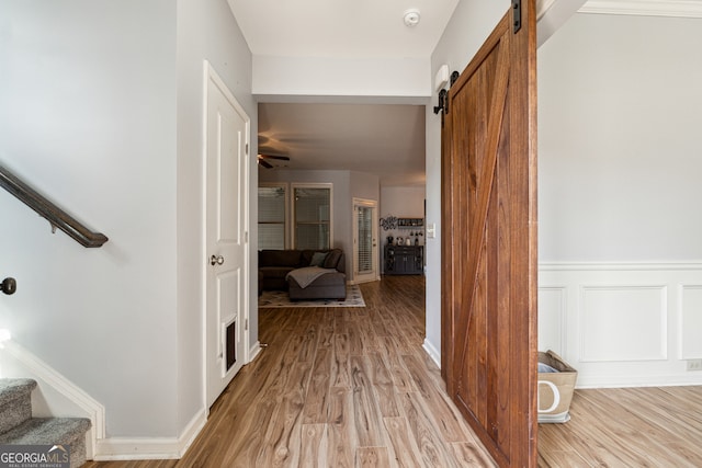 hall with a wainscoted wall, stairs, light wood-style floors, and a barn door