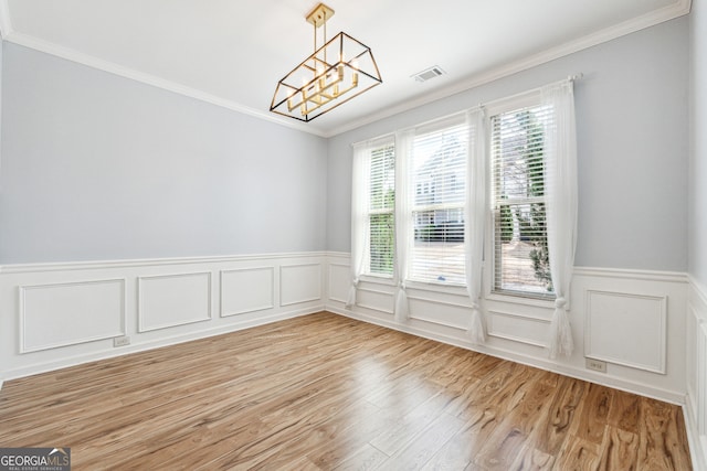 unfurnished dining area with a wainscoted wall, light wood-style floors, a chandelier, and crown molding