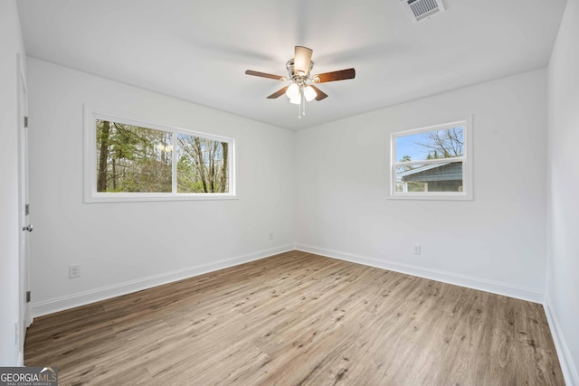 spare room with a ceiling fan, wood finished floors, visible vents, and baseboards