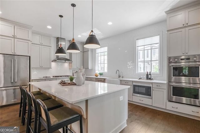 385 Rowes Cir, Alpharetta, GA 30009 - kitchen with appliances with stainless steel finishes, wall chimney exhaust hood, a kitchen island, light countertops, and dark wood-style flooring