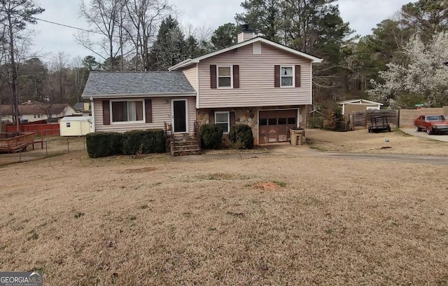 tri-level home with fence, roof with shingles, a chimney, stone siding, and an attached garage