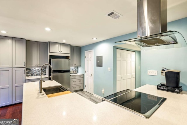 kitchen featuring visible vents, gray cabinetry, stovetop, island exhaust hood, and a sink