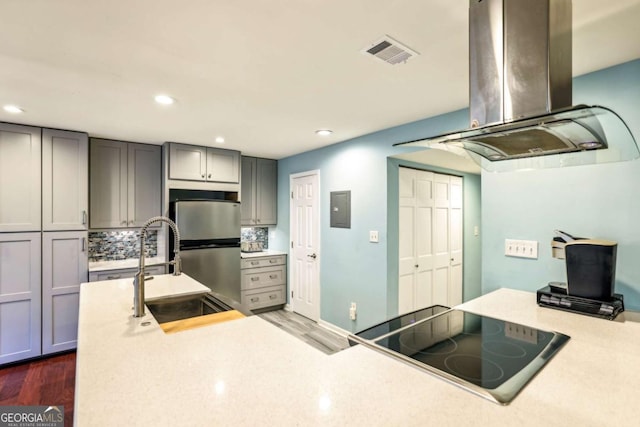kitchen with visible vents, a sink, island range hood, stovetop, and gray cabinets