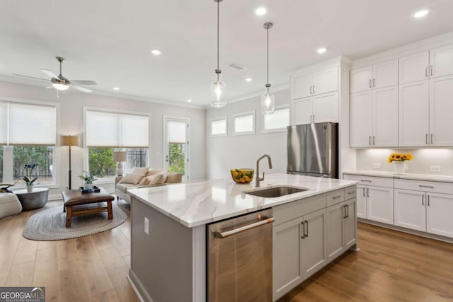 kitchen with a center island with sink, light wood finished floors, a sink, appliances with stainless steel finishes, and open floor plan