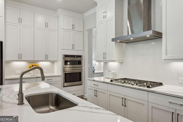 kitchen with a sink, tasteful backsplash, stainless steel appliances, wall chimney exhaust hood, and white cabinets