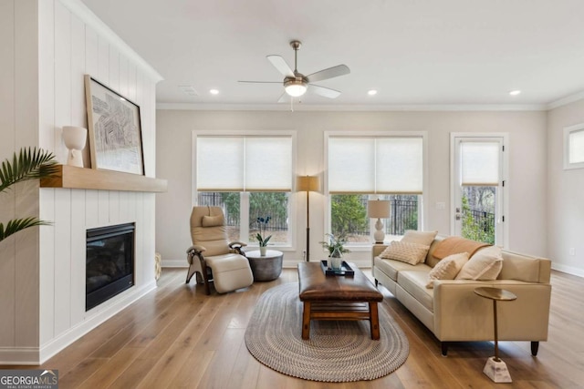 living room with wood finished floors, baseboards, ceiling fan, ornamental molding, and a glass covered fireplace