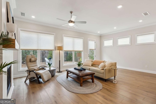 living room with hardwood / wood-style floors, baseboards, visible vents, ceiling fan, and crown molding