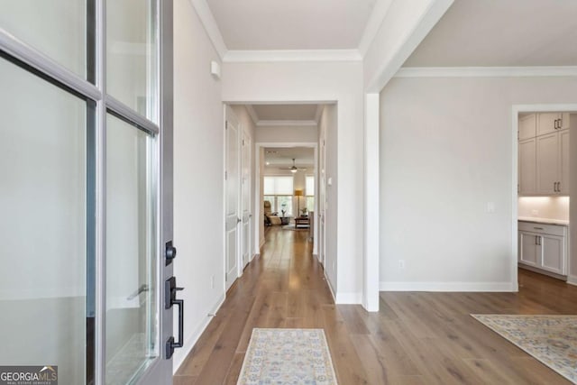 corridor featuring baseboards, light wood finished floors, and ornamental molding