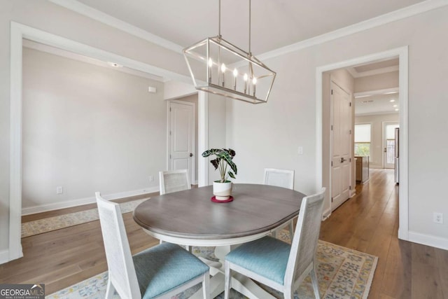 dining area with a chandelier, baseboards, wood-type flooring, and ornamental molding