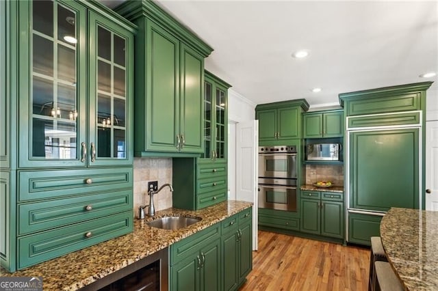 kitchen with tasteful backsplash, a sink, light wood-type flooring, appliances with stainless steel finishes, and green cabinetry