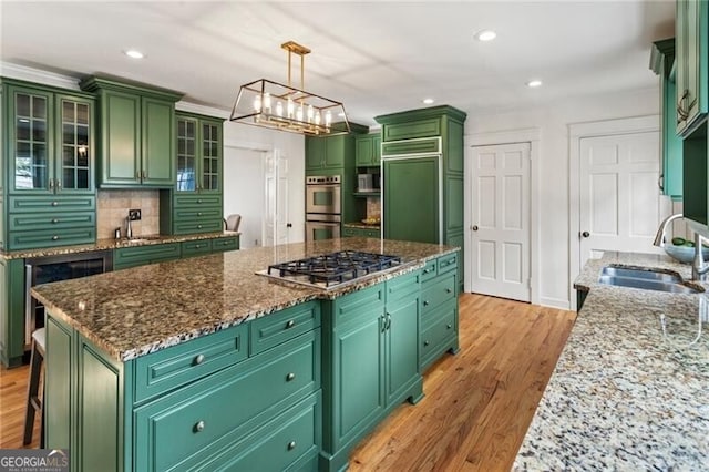 kitchen with a kitchen island, beverage cooler, light wood-type flooring, appliances with stainless steel finishes, and a sink