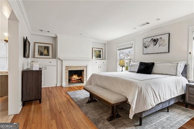 bedroom featuring visible vents, a fireplace with flush hearth, light wood-style flooring, and crown molding