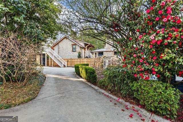 view of front of house featuring stairs, stone siding, driveway, and fence