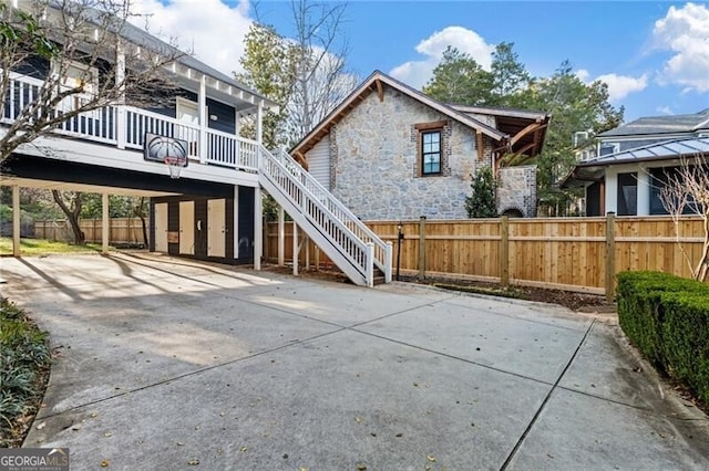 back of house with fence, stairs, a carport, stone siding, and driveway