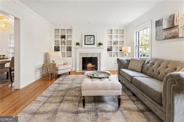 living room featuring built in shelves, a fireplace with flush hearth, wood finished floors, crown molding, and baseboards