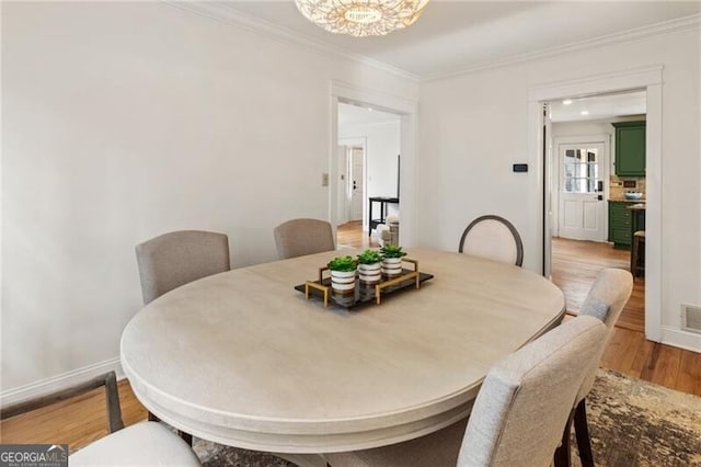 dining space featuring light wood finished floors, an inviting chandelier, crown molding, and baseboards