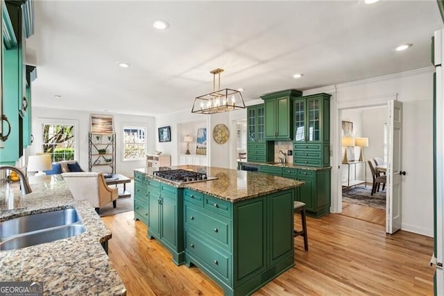 kitchen with a kitchen island, green cabinets, light wood-style flooring, stainless steel gas stovetop, and a sink