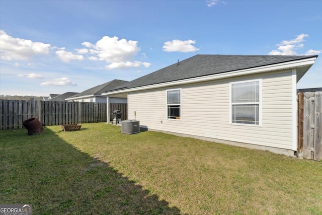 rear view of house featuring a lawn, cooling unit, a fenced backyard, and roof with shingles