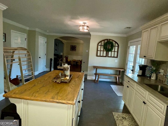 kitchen with a sink, arched walkways, butcher block countertops, and crown molding