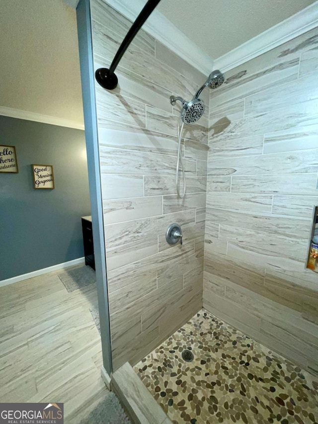 full bathroom featuring a tile shower, crown molding, and baseboards