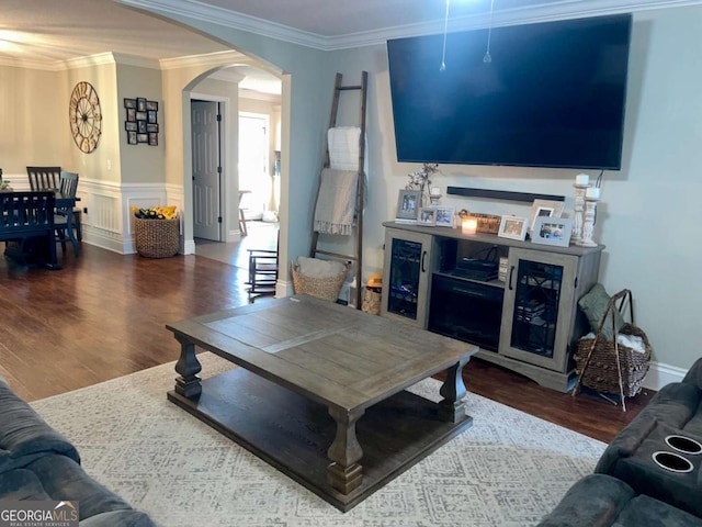 living area featuring arched walkways, a wainscoted wall, wood finished floors, and ornamental molding