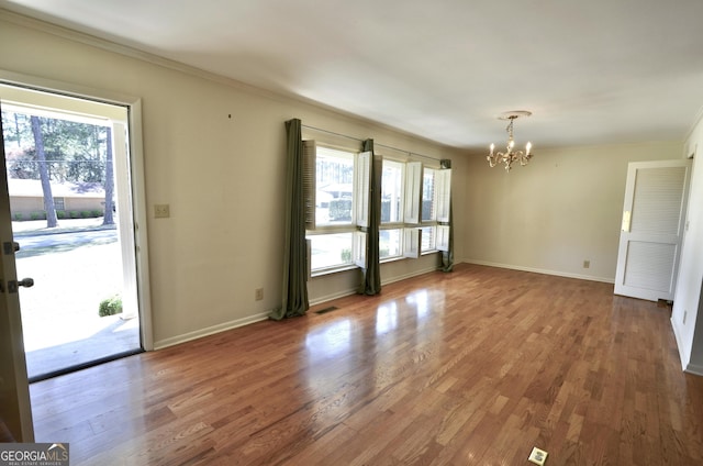 unfurnished room with a healthy amount of sunlight, baseboards, an inviting chandelier, and wood finished floors