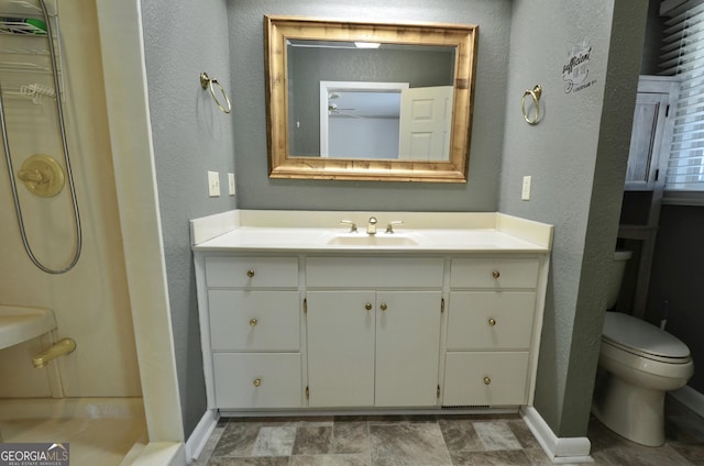 bathroom with vanity, baseboards, ceiling fan, toilet, and a textured wall