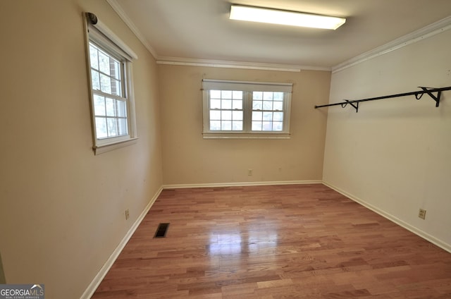 unfurnished room featuring visible vents, wood finished floors, baseboards, and ornamental molding