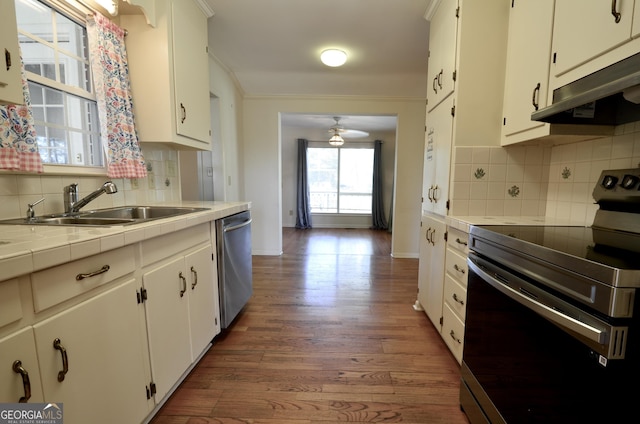 kitchen featuring crown molding, under cabinet range hood, tile countertops, appliances with stainless steel finishes, and a sink