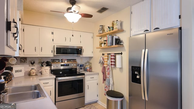 kitchen featuring visible vents, a sink, stainless steel appliances, white cabinets, and ceiling fan