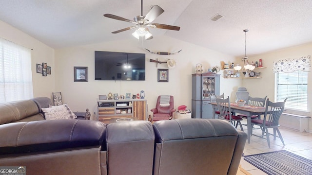 living area featuring visible vents, lofted ceiling, ceiling fan with notable chandelier, light tile patterned flooring, and a textured ceiling